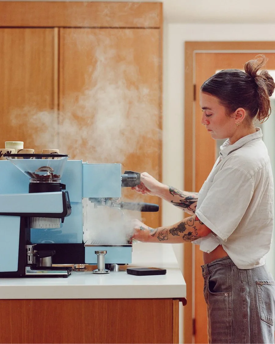 Barista steaming milk on a pastel blue espresso machine