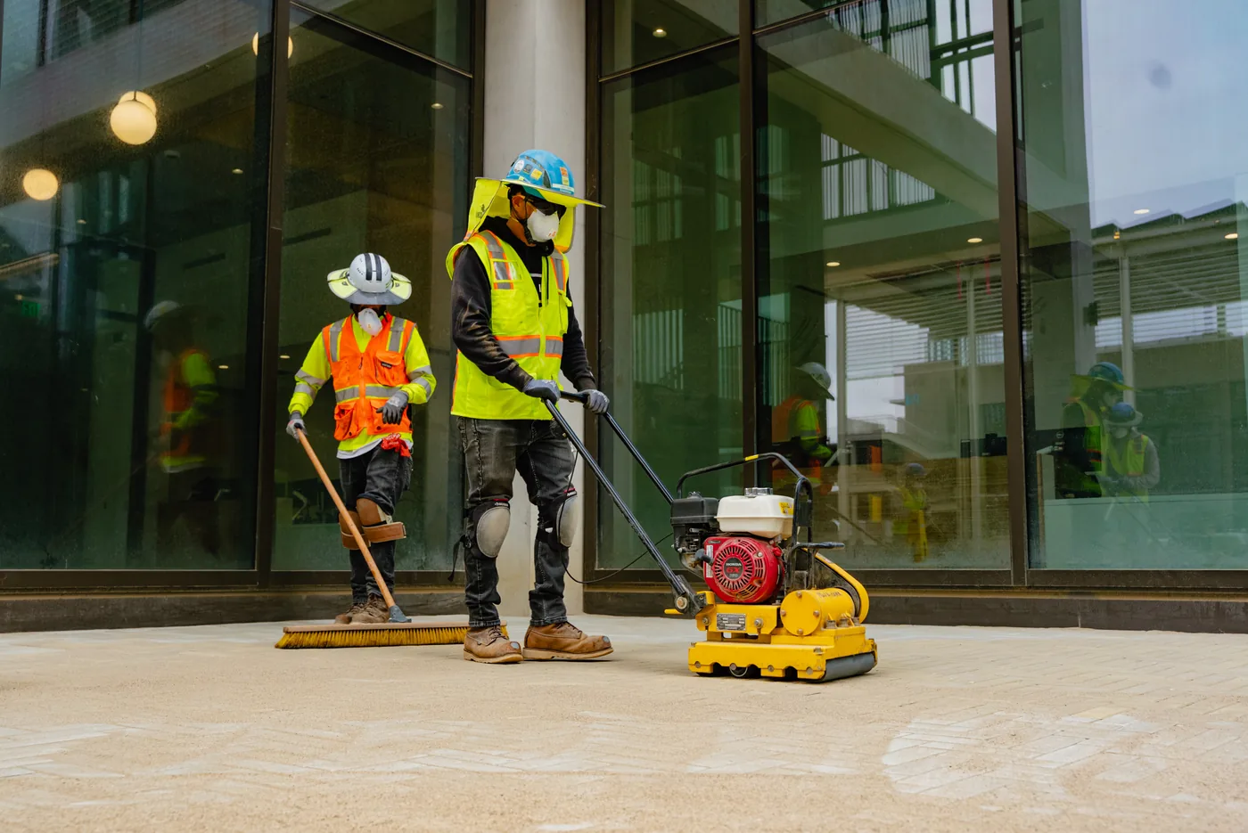 Crew finishing concrete with a Tomahawk power trowel outside a glass office building