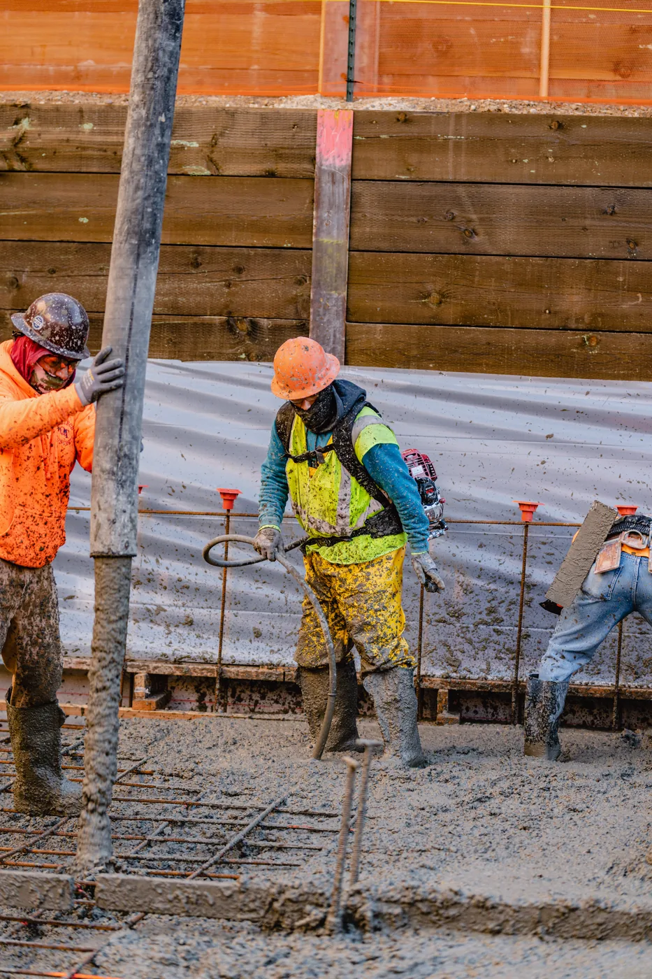 Crew placing concrete into wall forms against a shored embankment