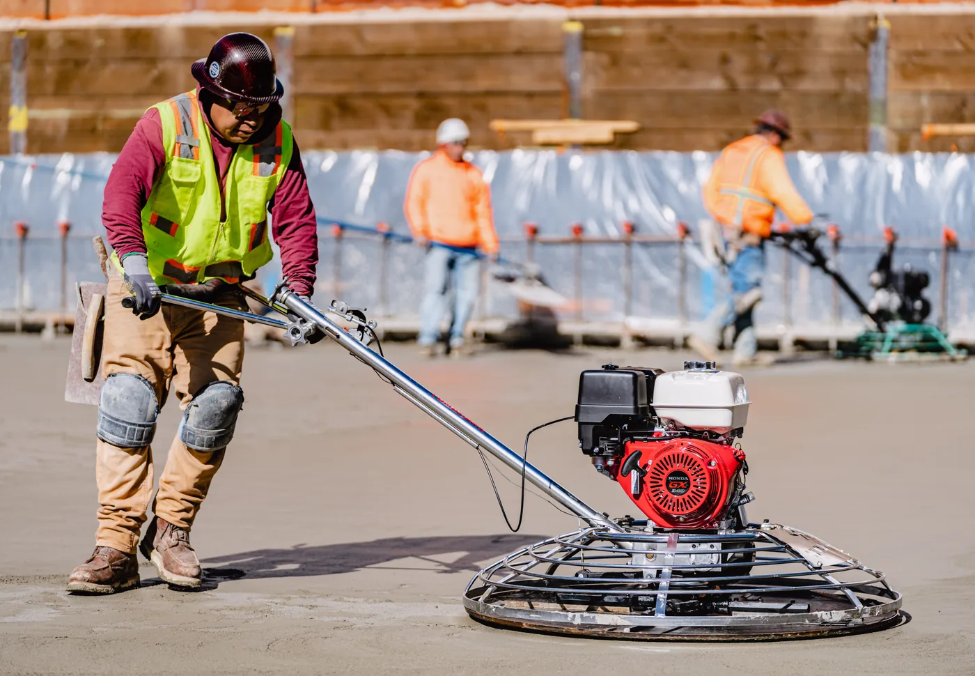 Finisher leaning into a Tomahawk ride-behind power trowel on wet concrete