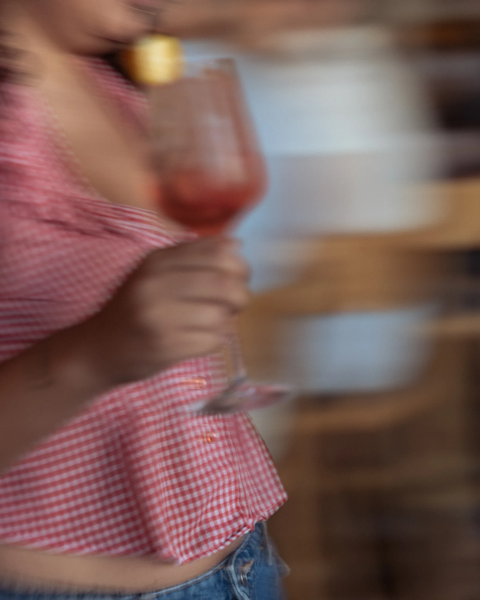 Motion-blurred frame of a guest in a gingham top raising a glass of wine