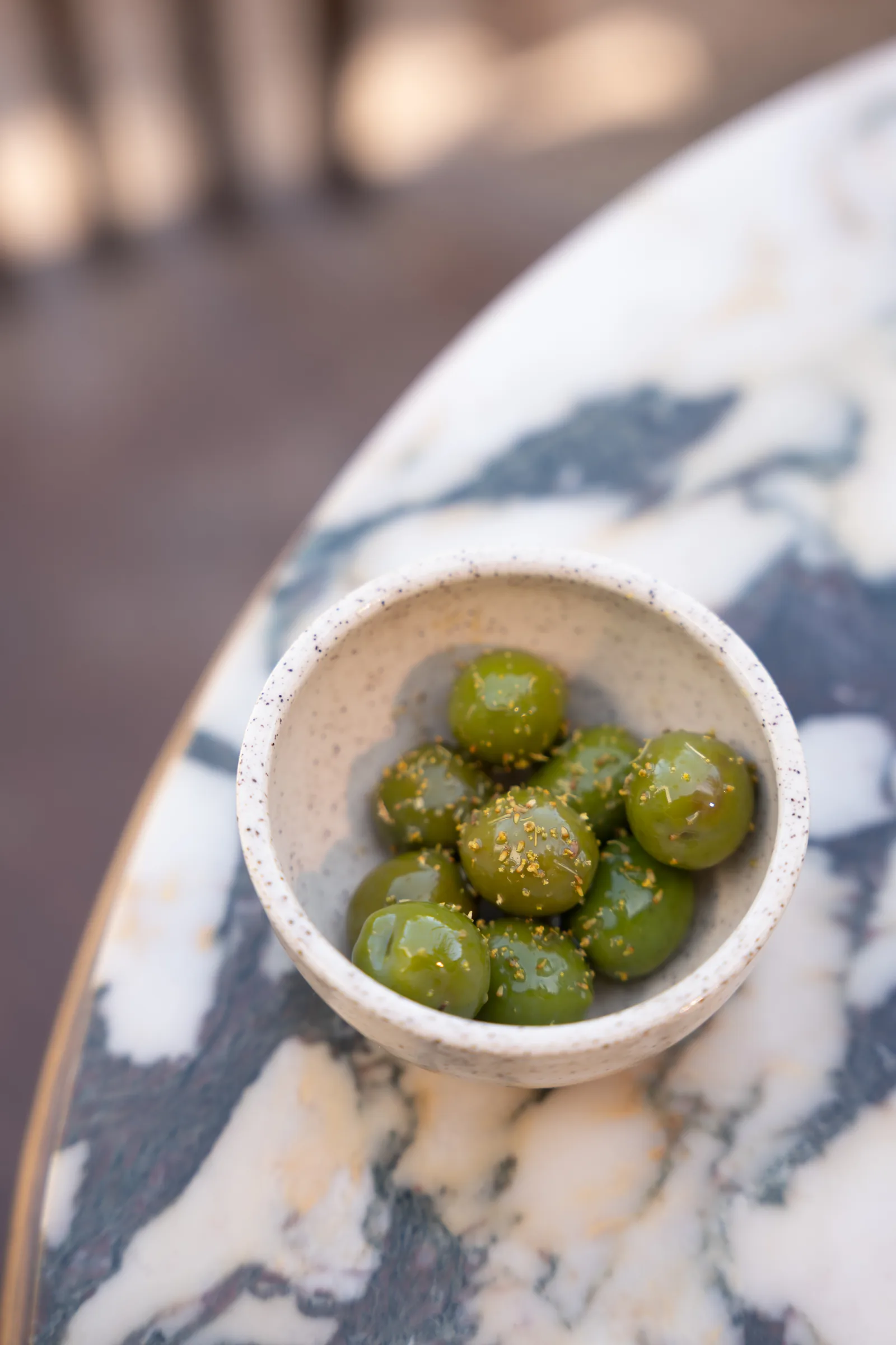 Marinated green olives in a speckled ceramic bowl on a marble table