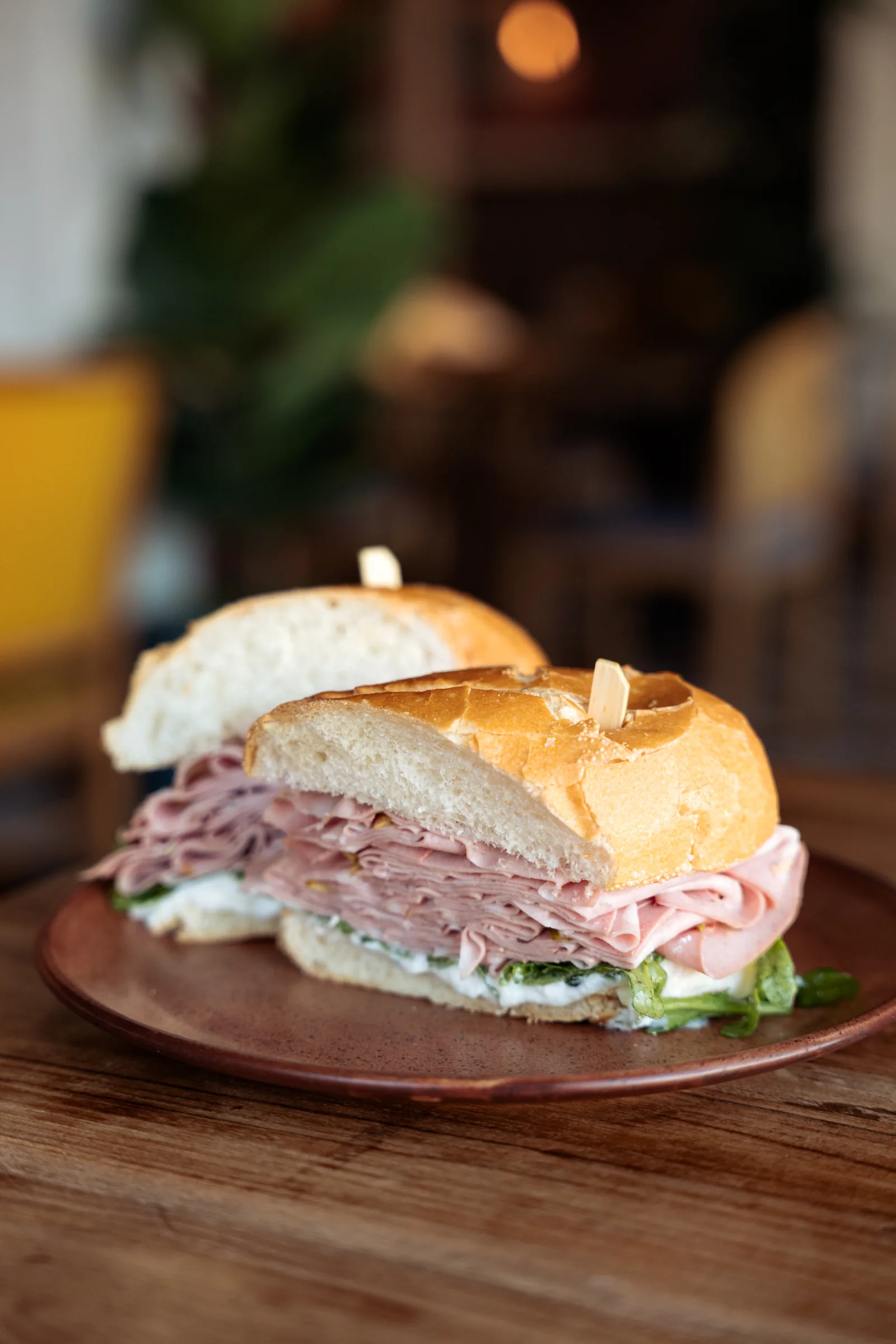 A mortadella sandwich on a clay plate on a wooden table