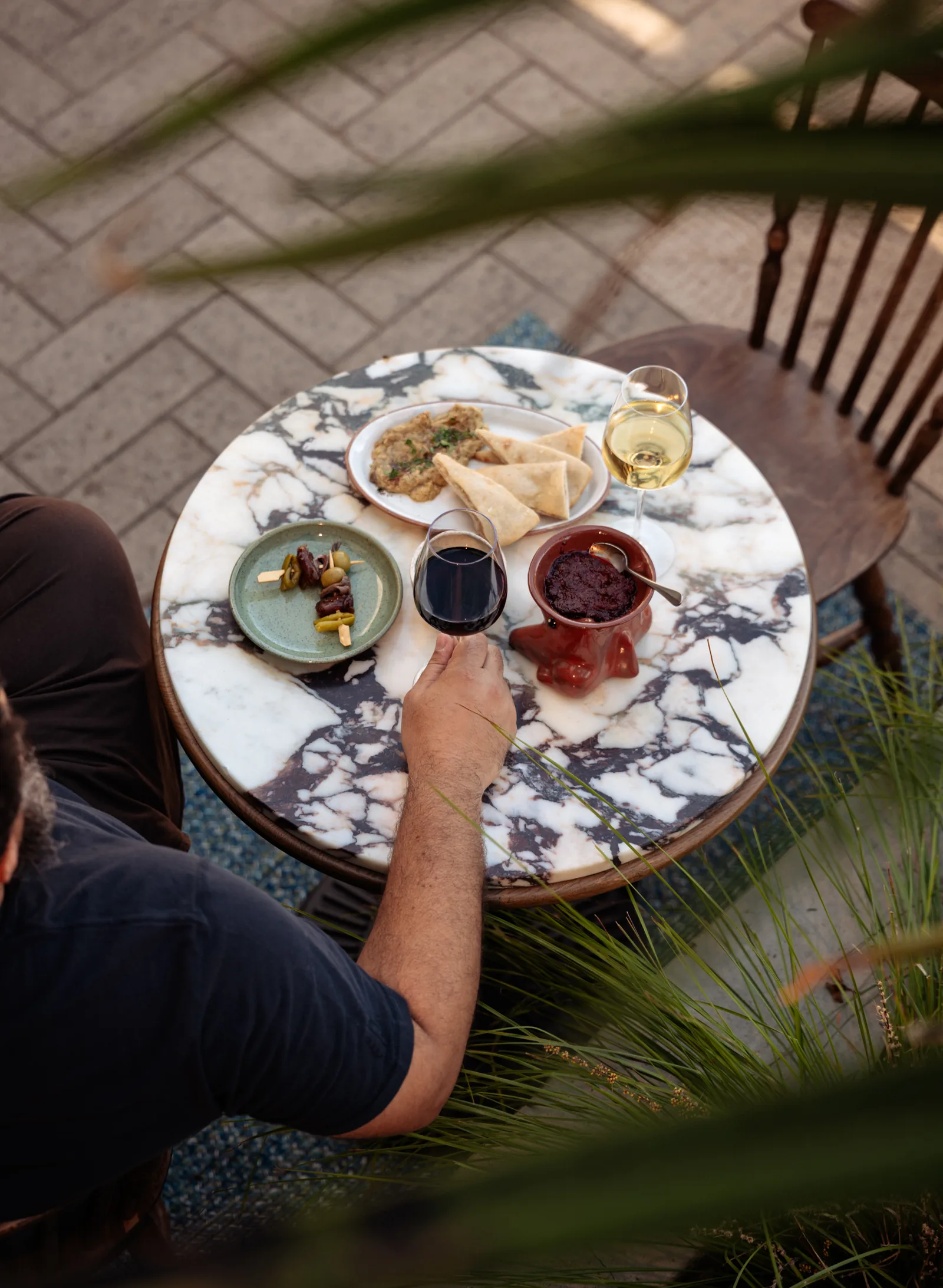Overhead view of a guest at a marble patio table with wine and small plates
