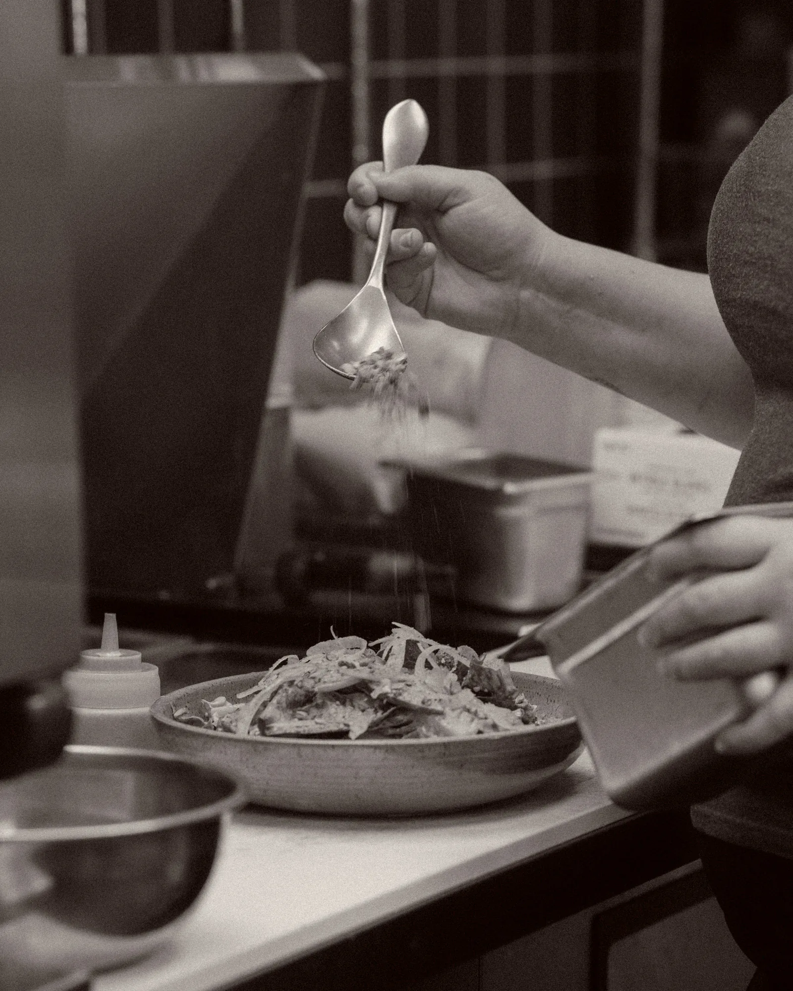 Black and white frame of a cook finishing a dish in the kitchen