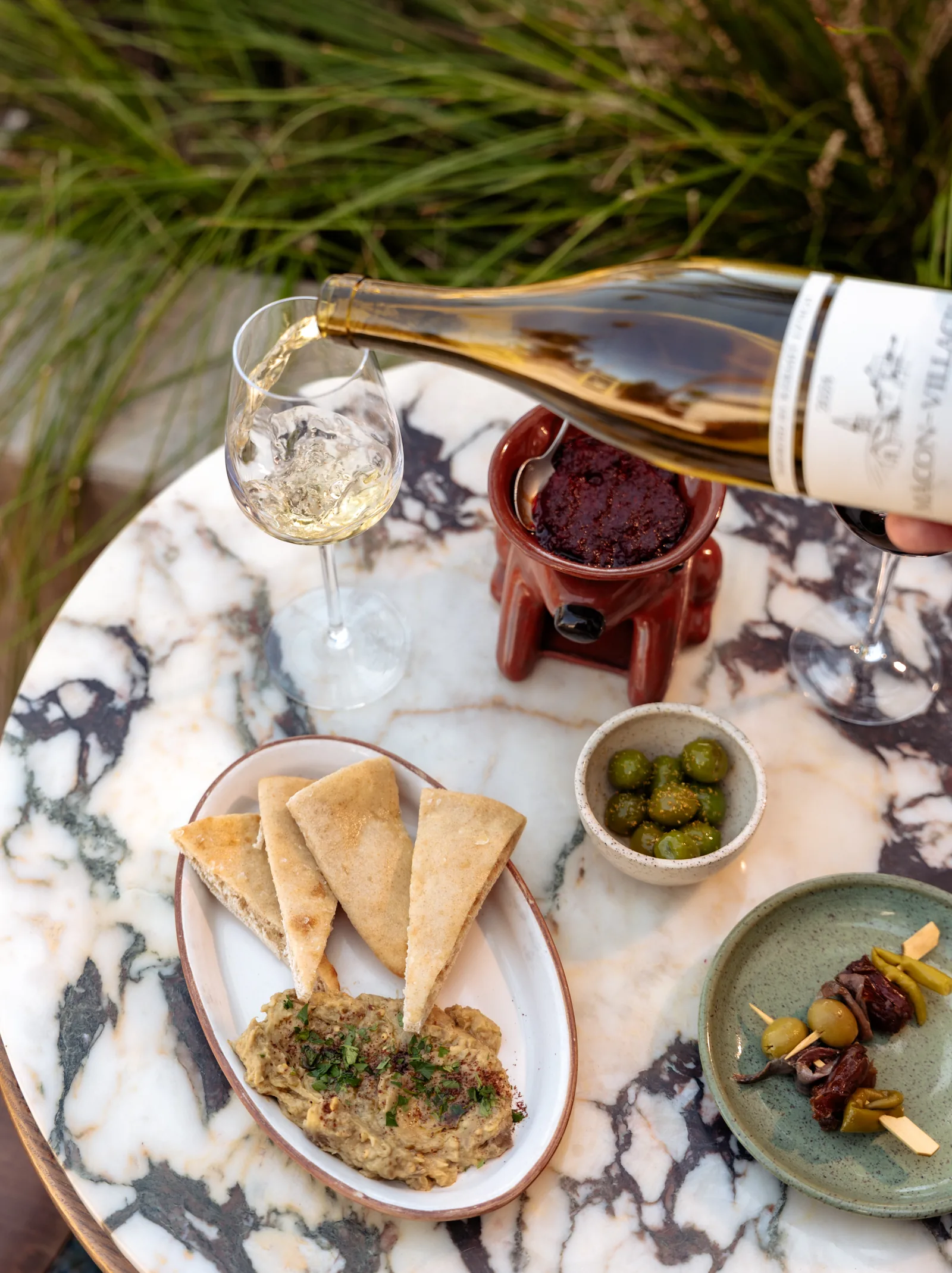 White wine being poured beside pita, dip and olives on a marble table