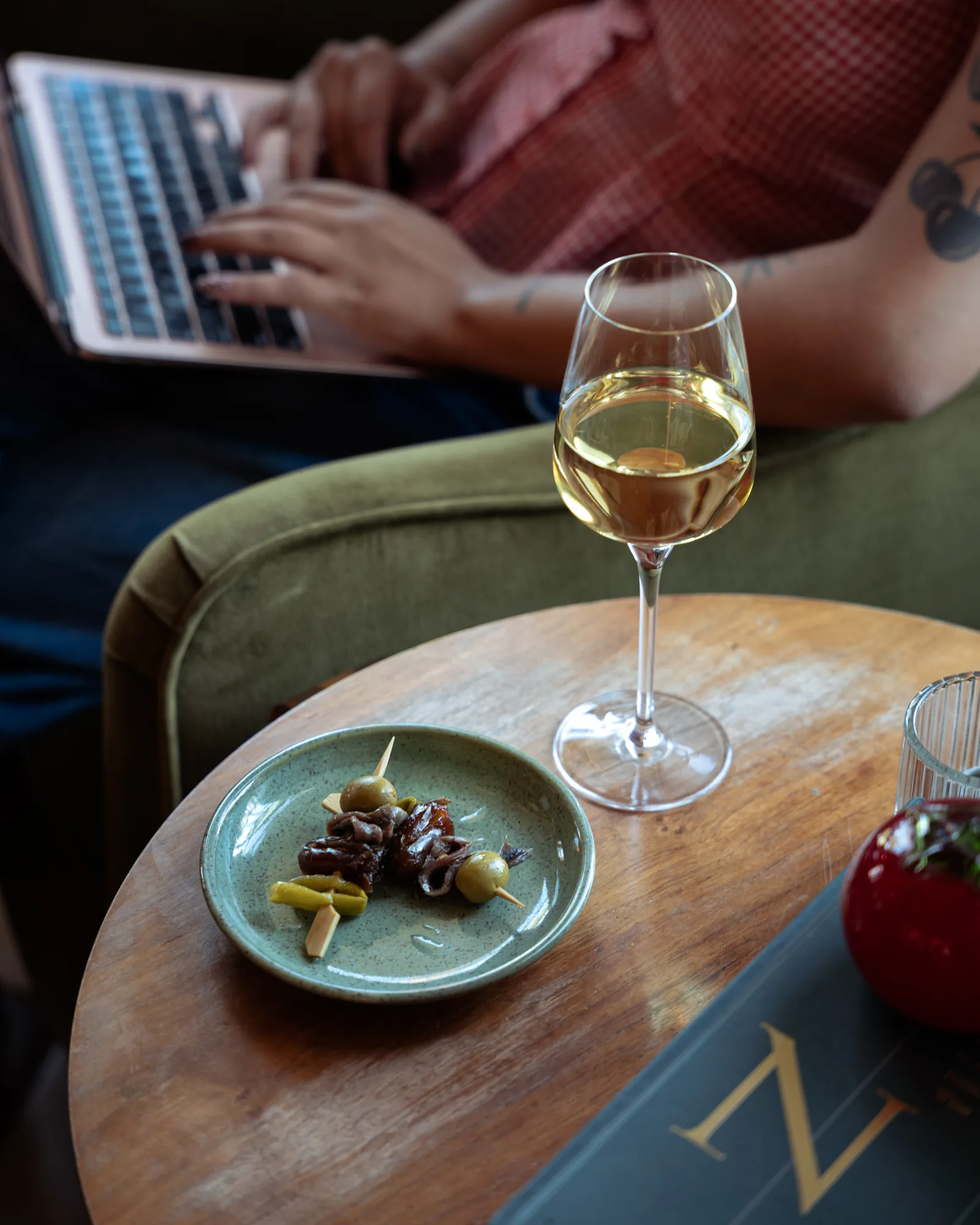 A glass of white wine and a plate of skewers on a side table beside a laptop