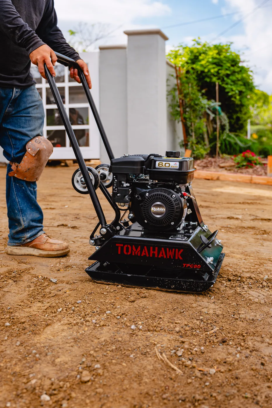 Operator walking a Tomahawk plate compactor over graded soil