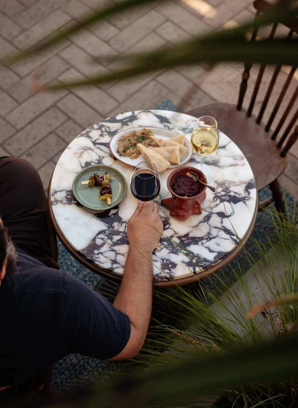 Overhead view of a marble patio table with red and white wine, baba ganoush and pita, olives and tapenade