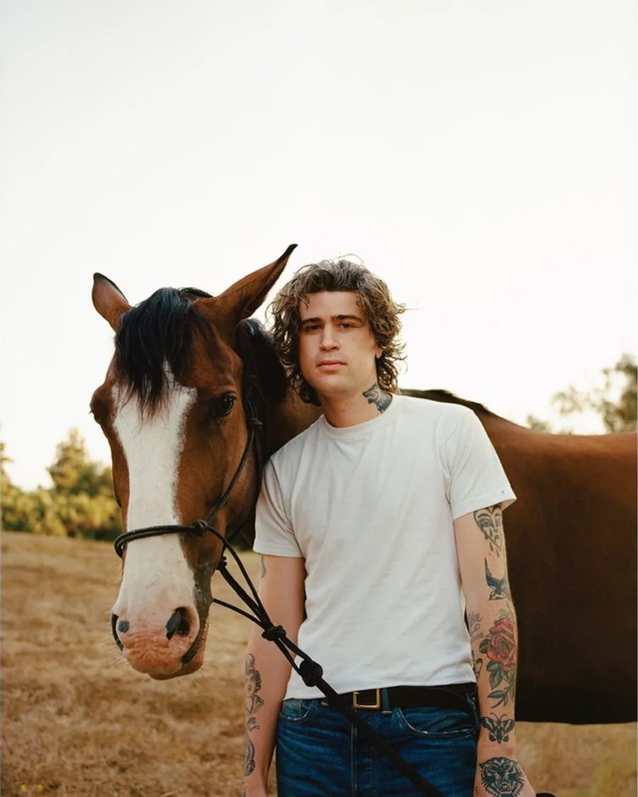 Portrait of a man with tattoos standing beside a horse