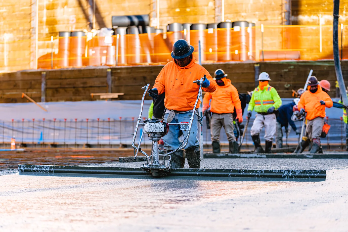 Screed operator working a wide slab with the finishing crew lined up behind him