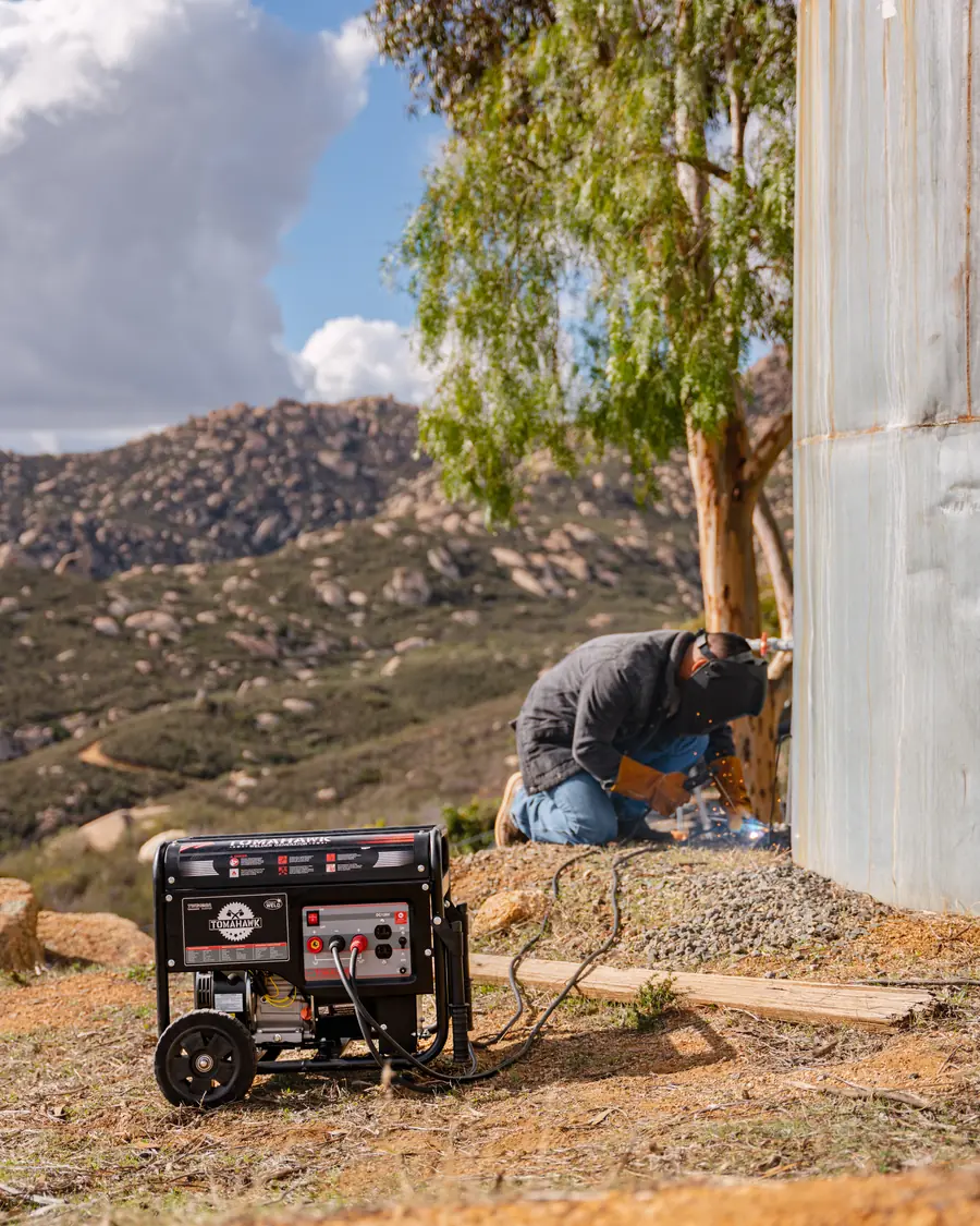 Tomahawk welder generator running on a hillside, welder crouched at a steel tank with the ridge behind them