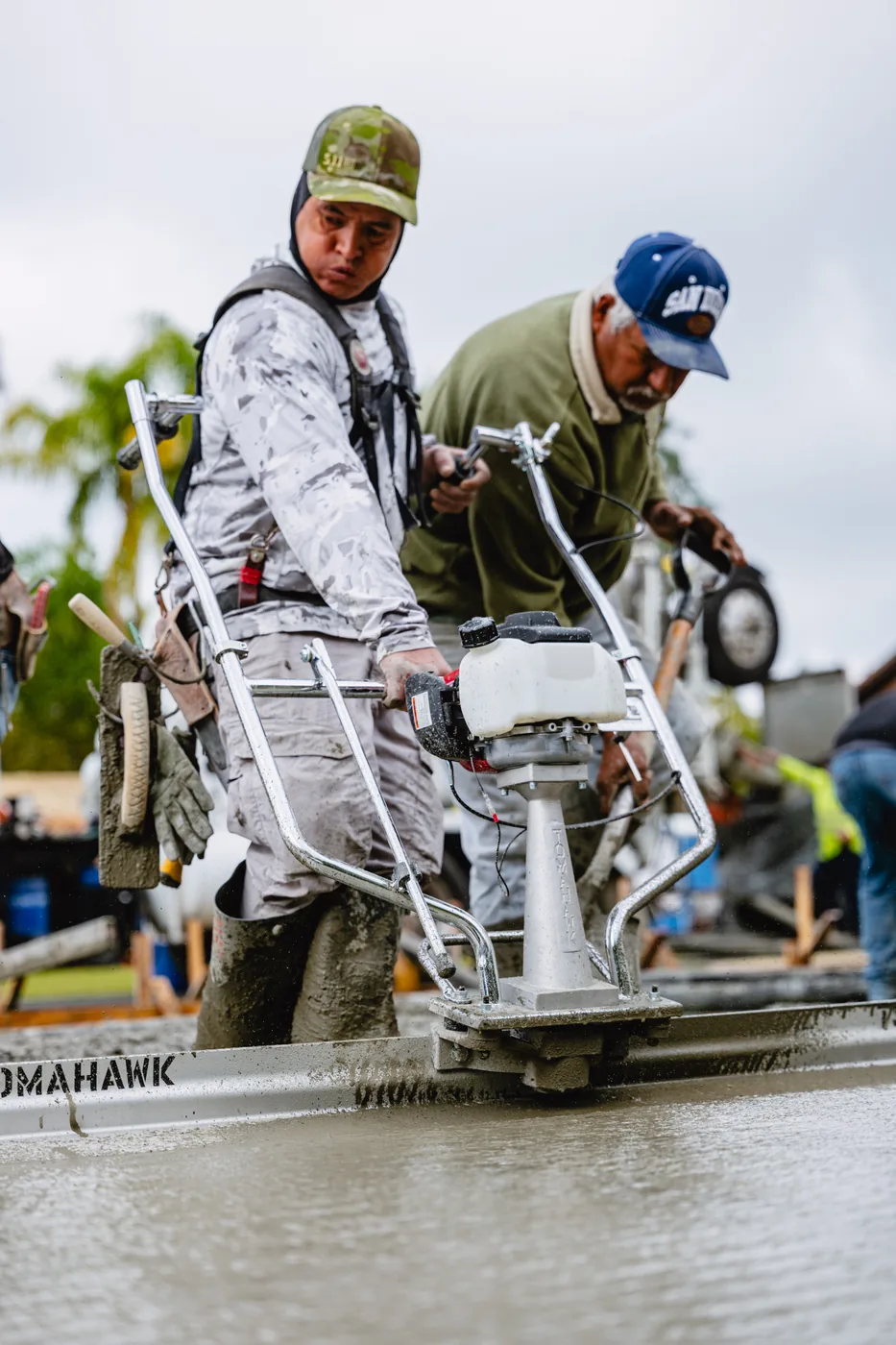 Two operators guiding a Tomahawk power screed across wet concrete