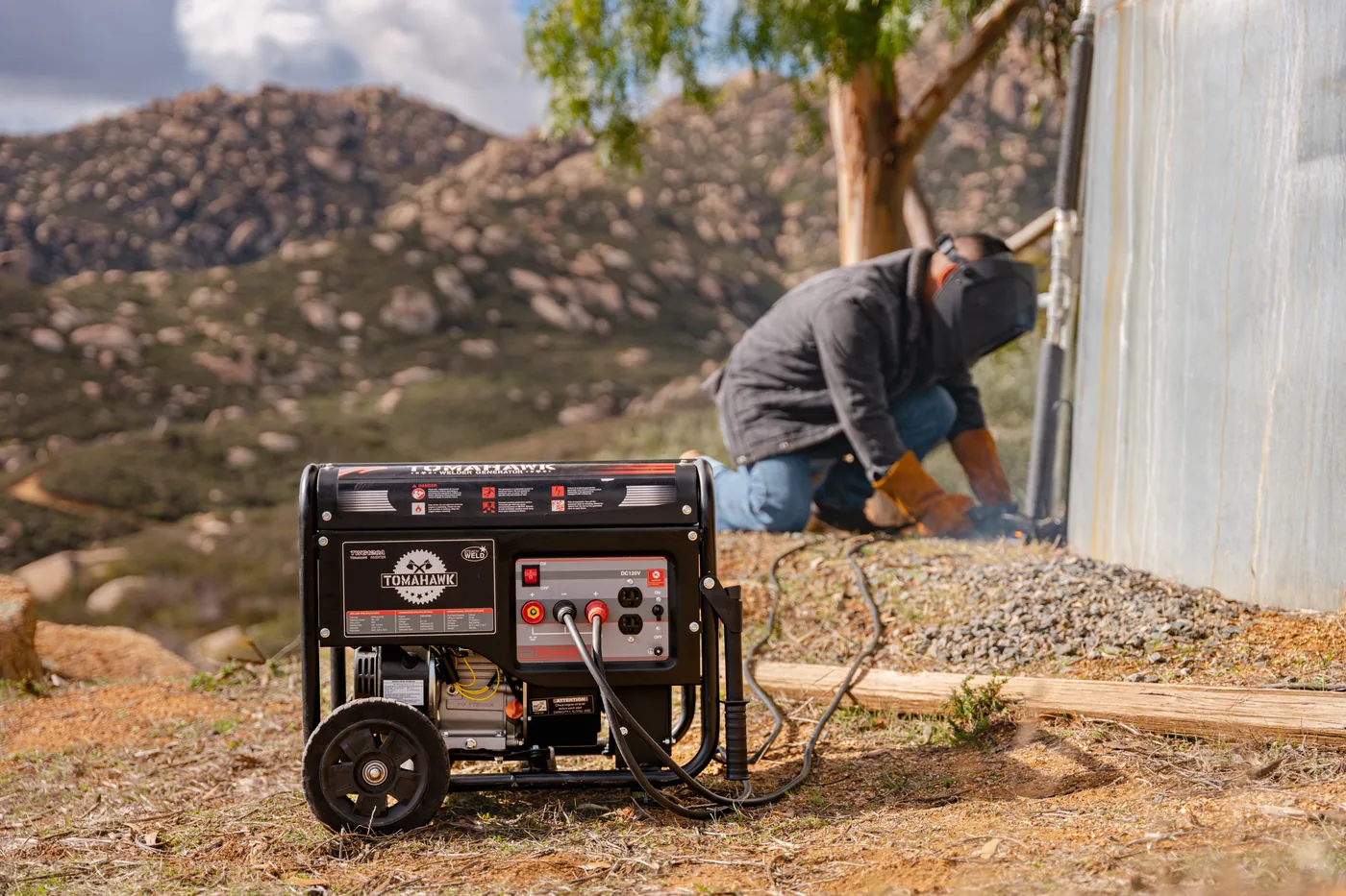 Welder generator on a hillside site with a welder at work behind it
