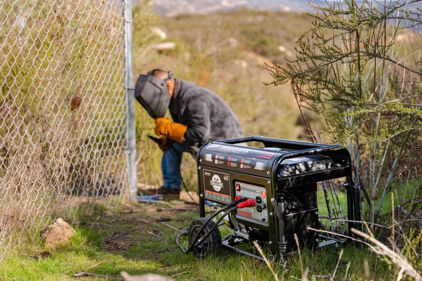Welder generator running beside a chain-link fence on a rural site