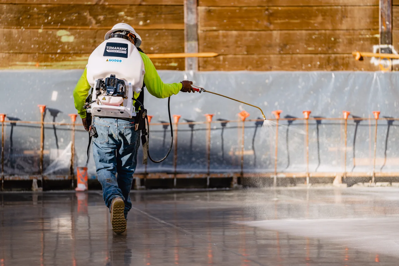 Worker crossing a finished slab with a backpack sprayer applying curing compound