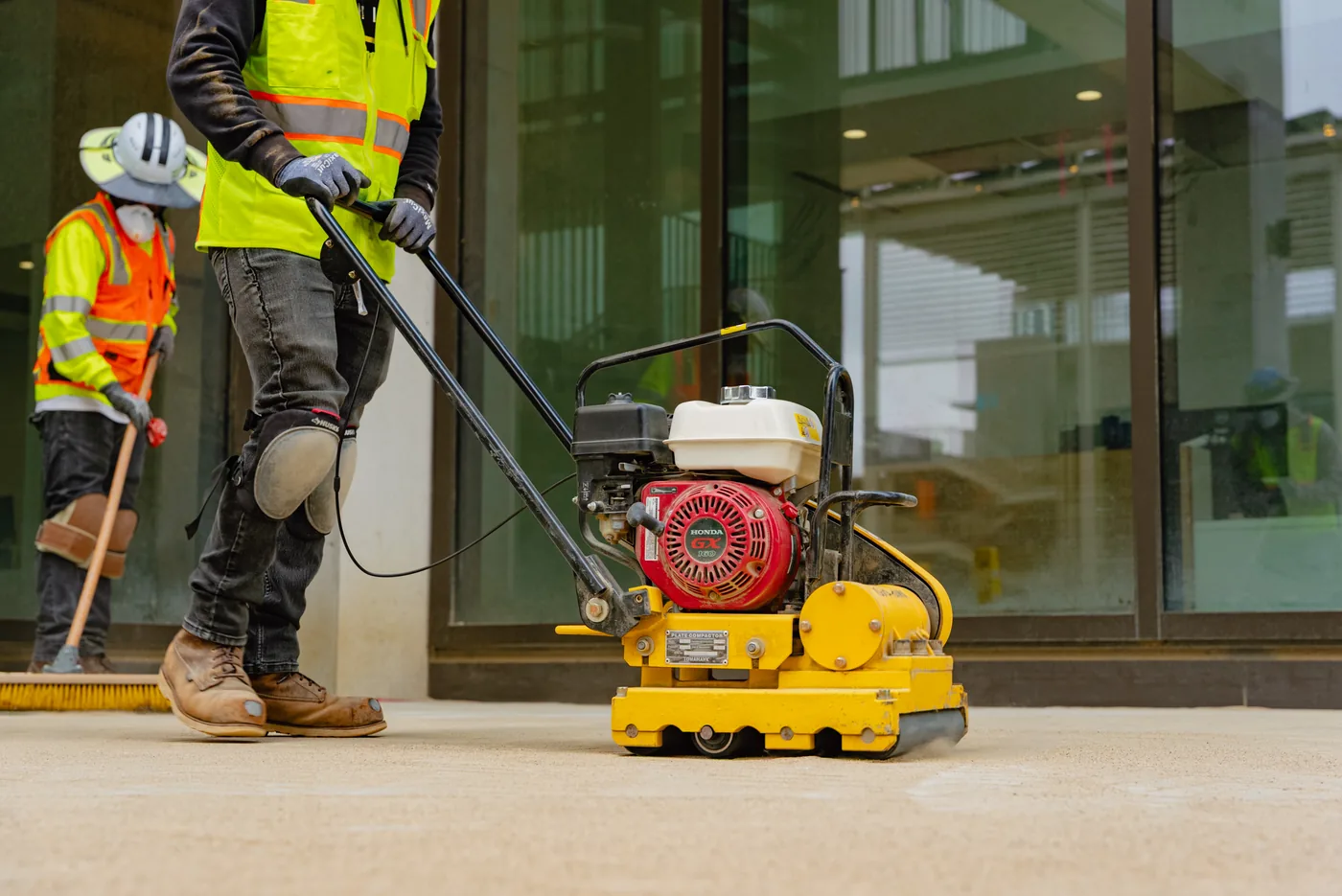 Worker running a Tomahawk plate compactor along a new walkway