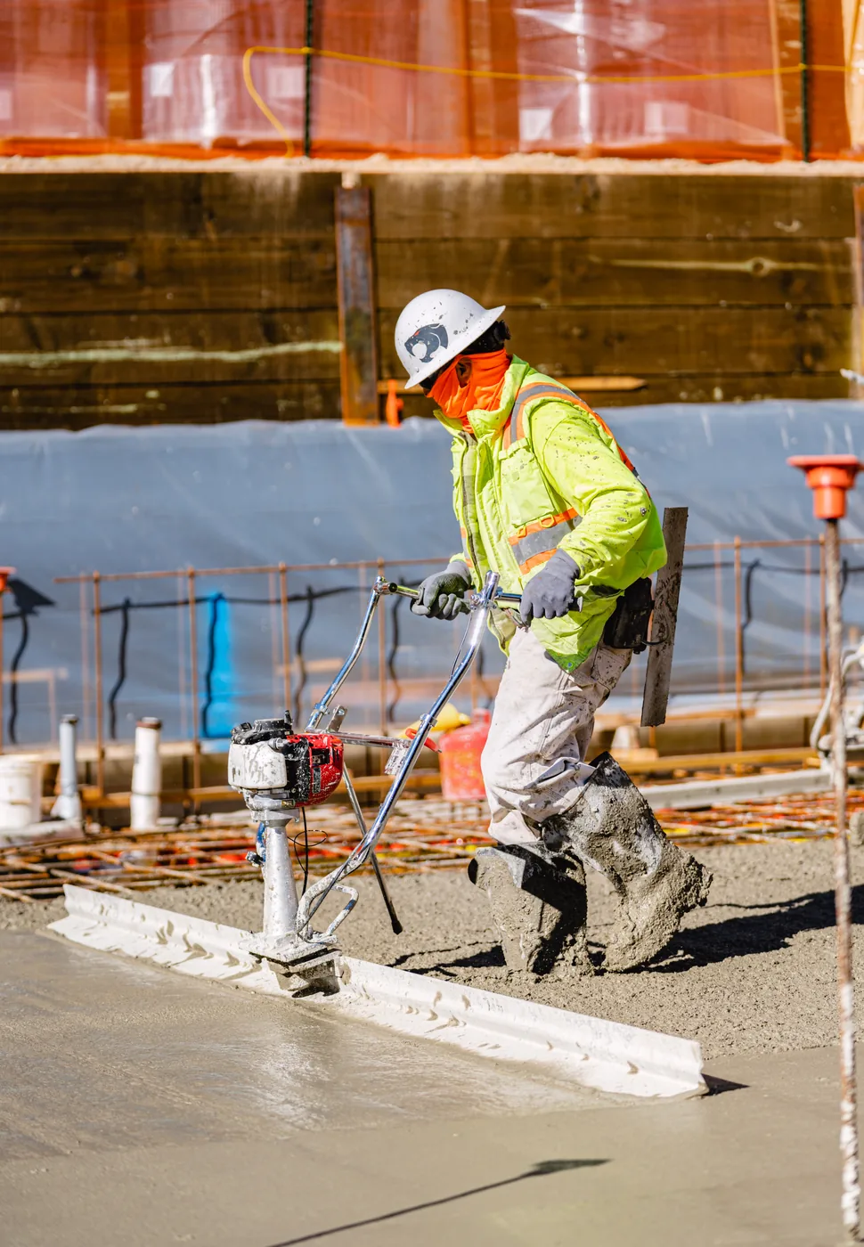 Worker steering a vibrating screed along the edge of a form
