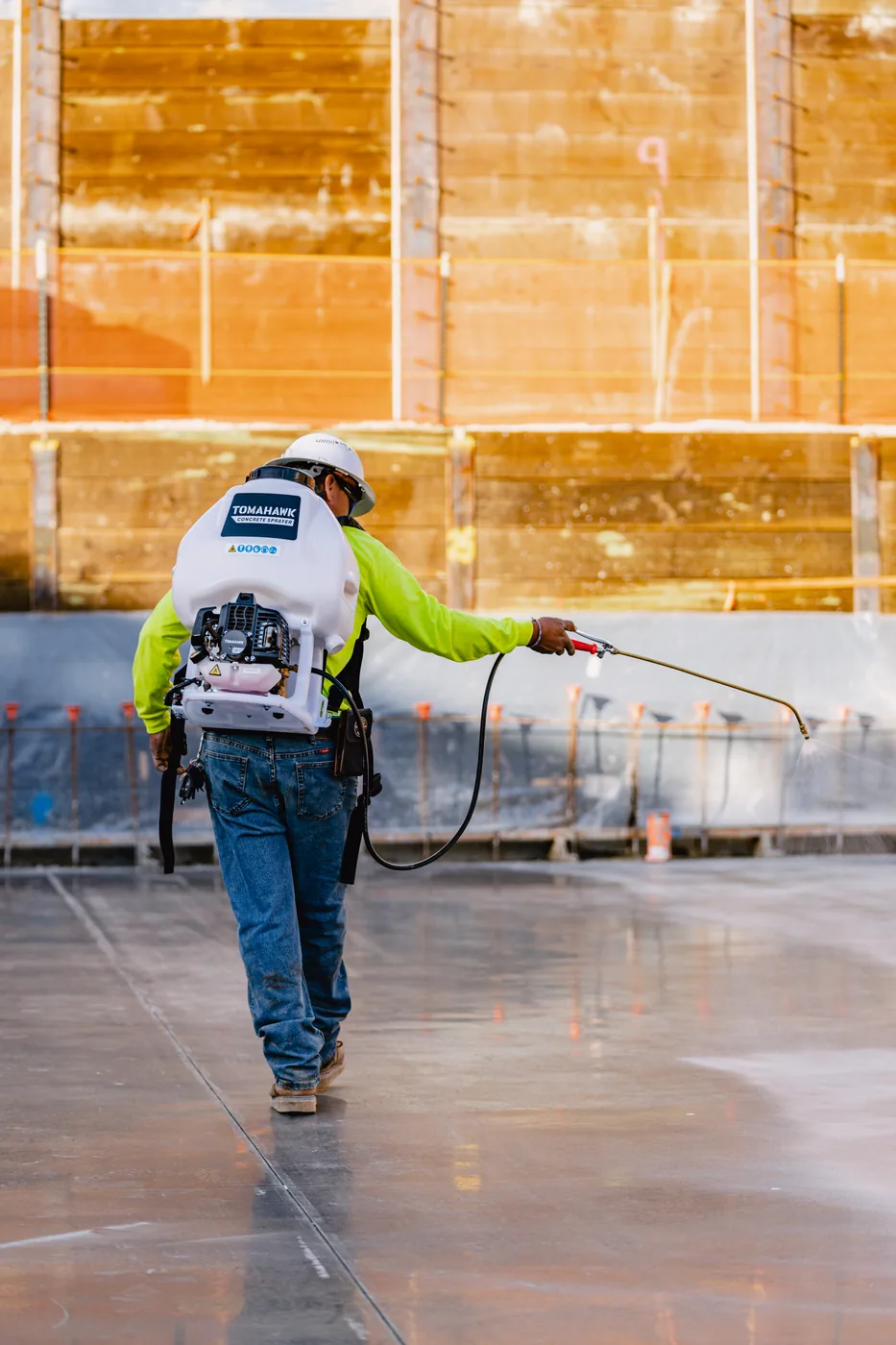 Worker walking away across a cured slab, backpack sprayer in hand